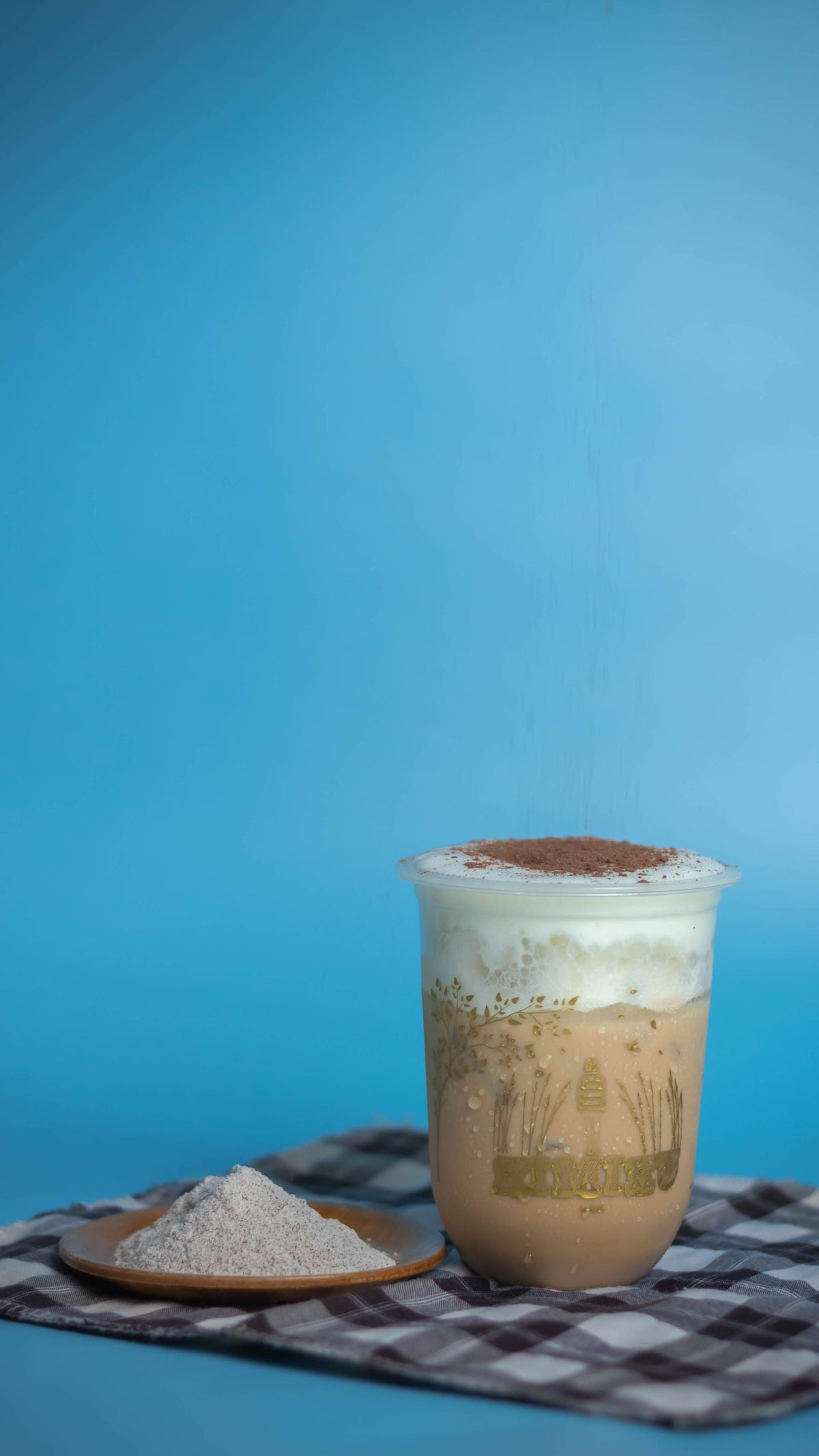 Delicious iced frappe topped with whipped cream and cocoa, served on a checkered cloth.
