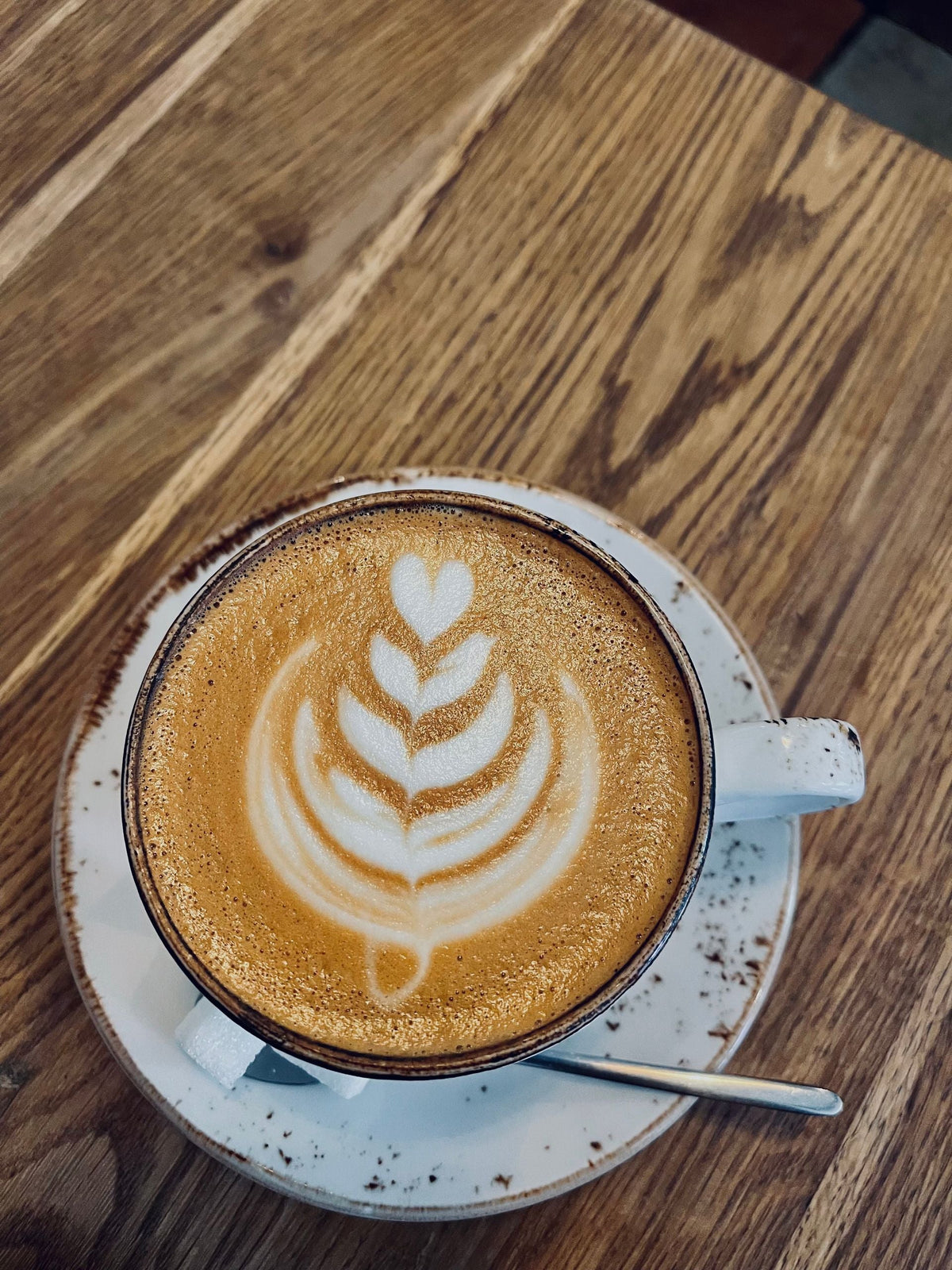 Top-down view of a latte with a heart-shaped foam art in a white cup on a wooden table.