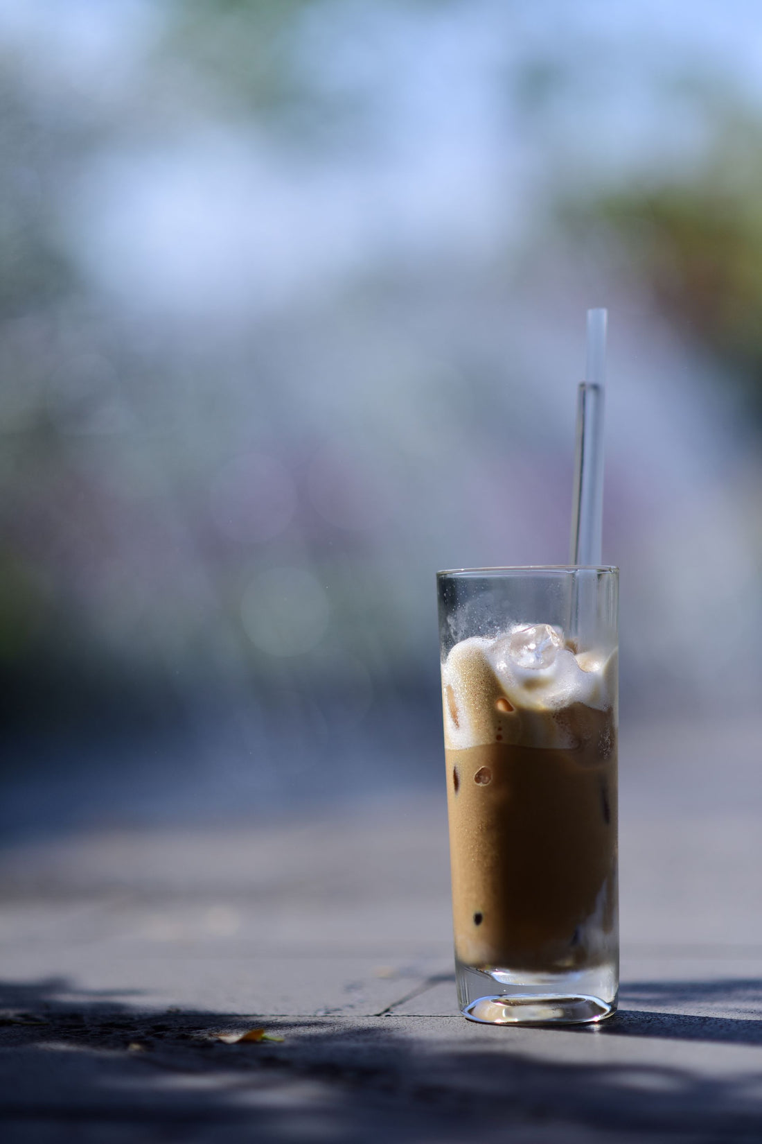 A refreshing glass of iced coffee with cream sits on a table under the clear blue sky, perfect for a summer day.