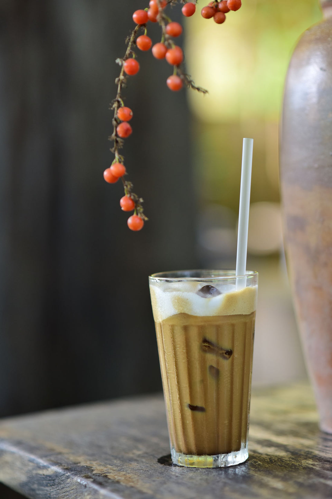 A refreshing iced coffee in a glass with ice cubes and a straw on a rustic table.
