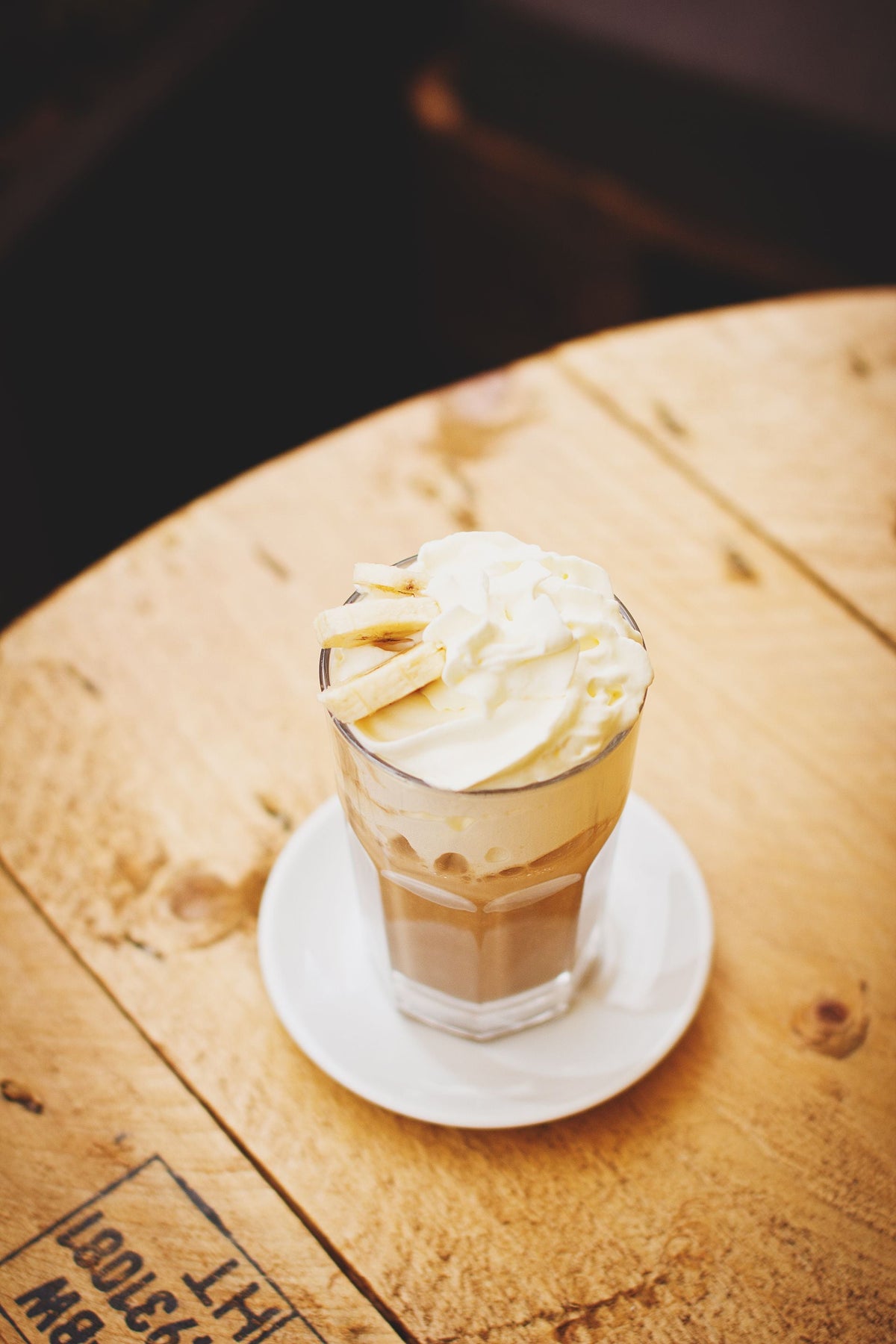 A creamy latte topped with whipped cream in a clear glass on a rustic wooden table, perfect for cozy coffee moments.