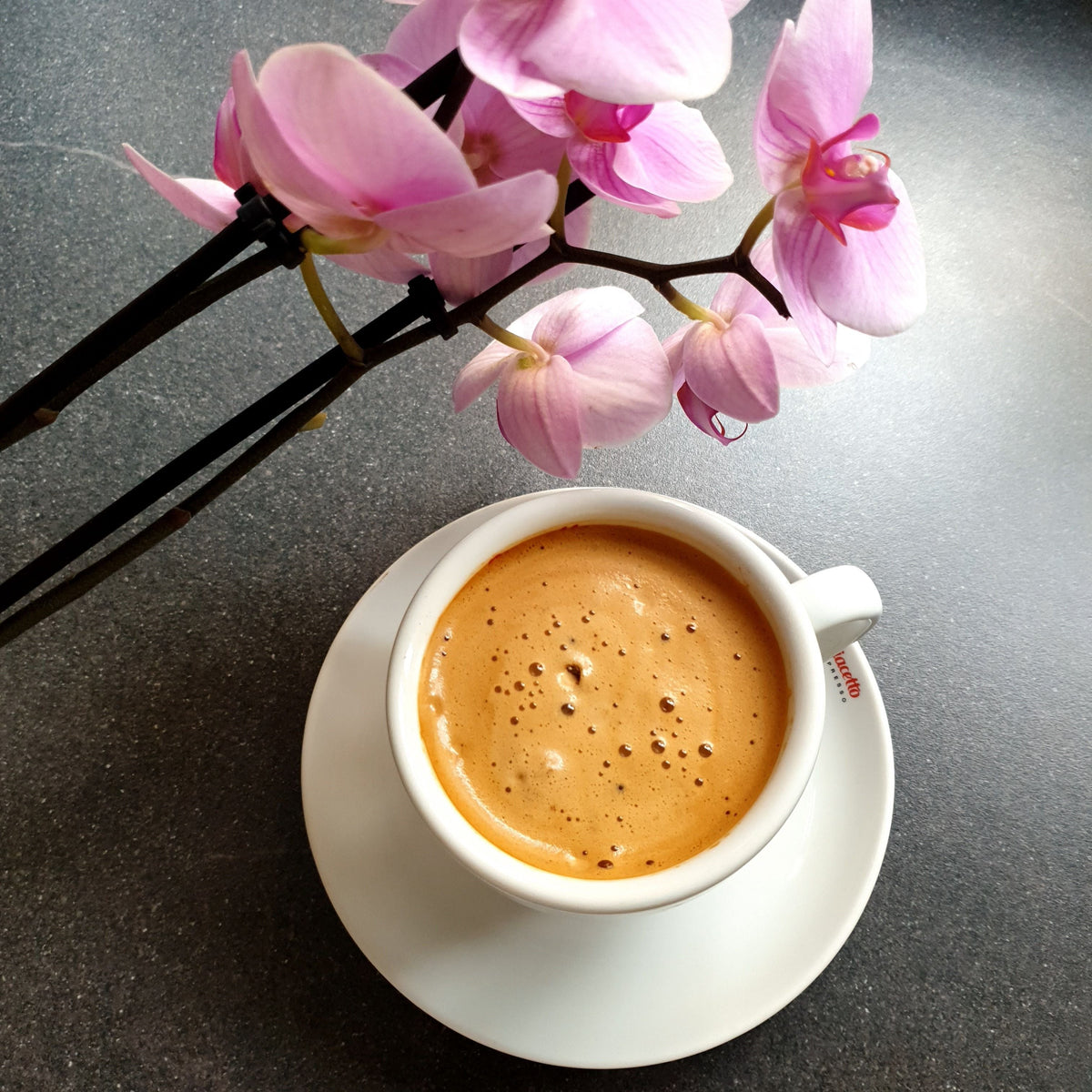 Cup of black coffee with crema beside pink orchid flowers