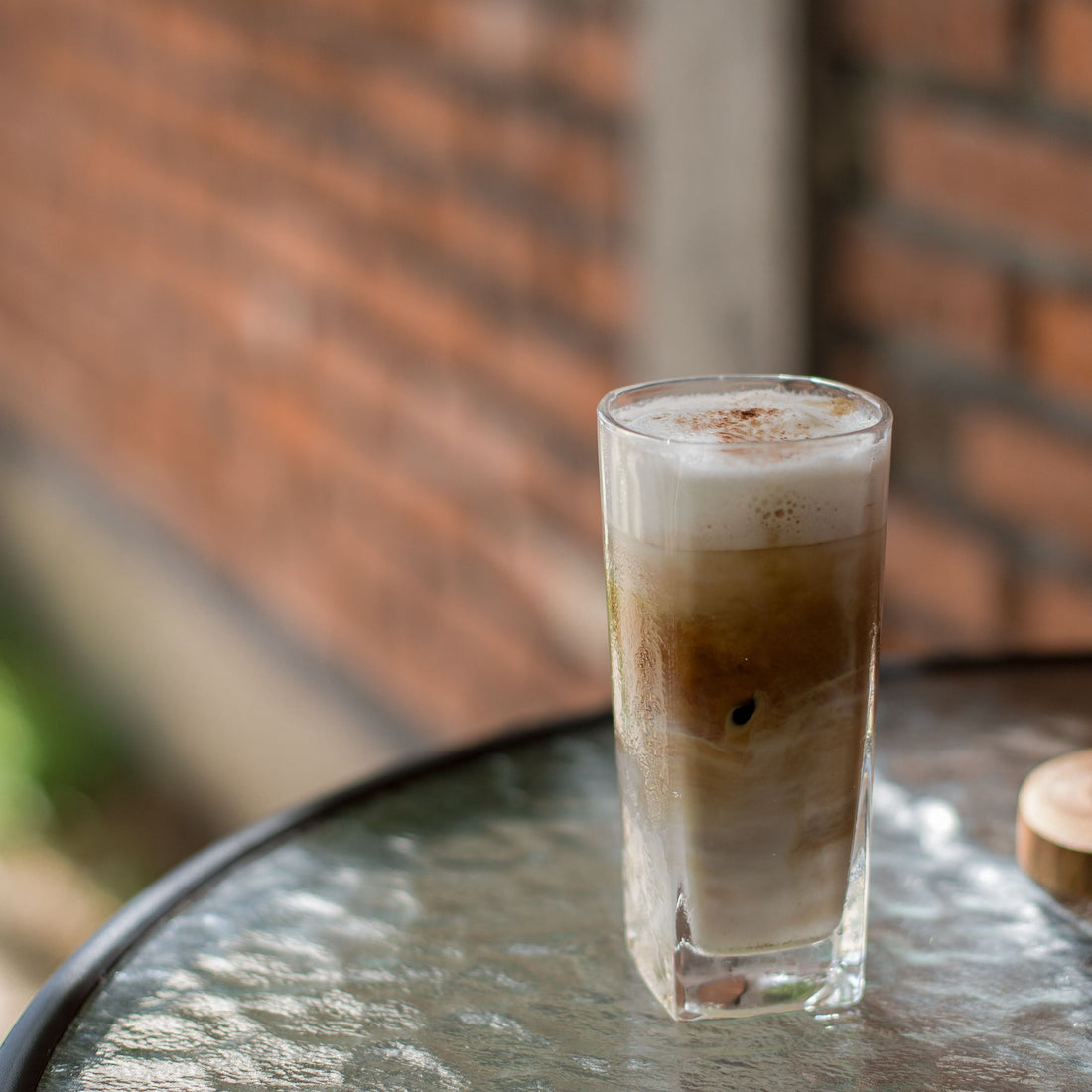 Iced coffee with milk and a foamy top in a tall glass on a table