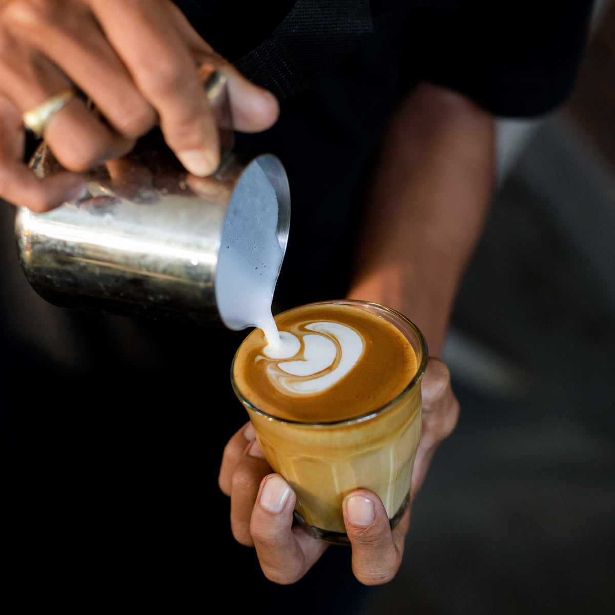 Steamed milk being poured into a glass of coffee