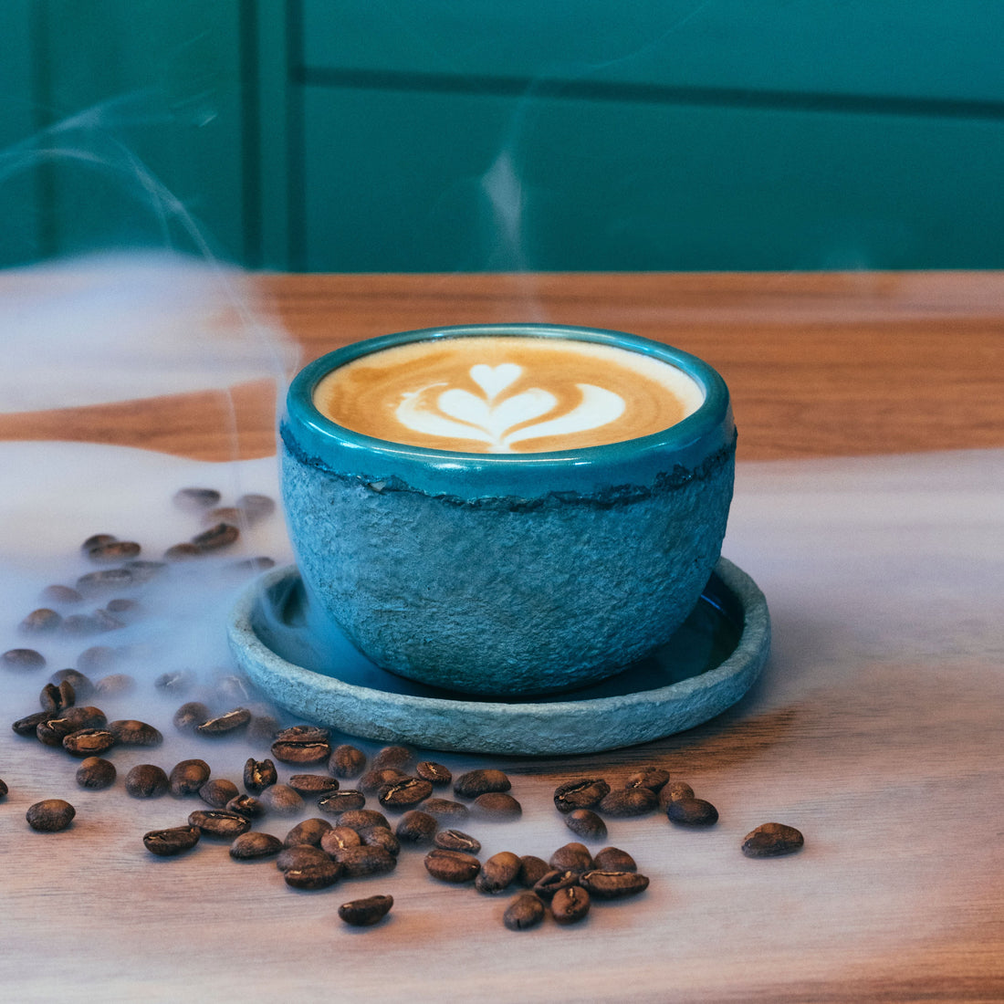 Coffee with latte art in a blue cup beside scattered coffee beans