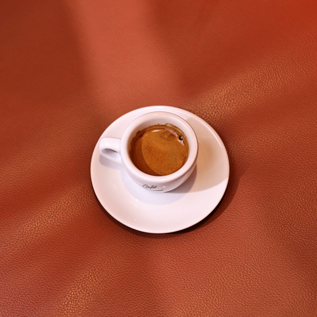 Small cup of espresso on a saucer against an orange background