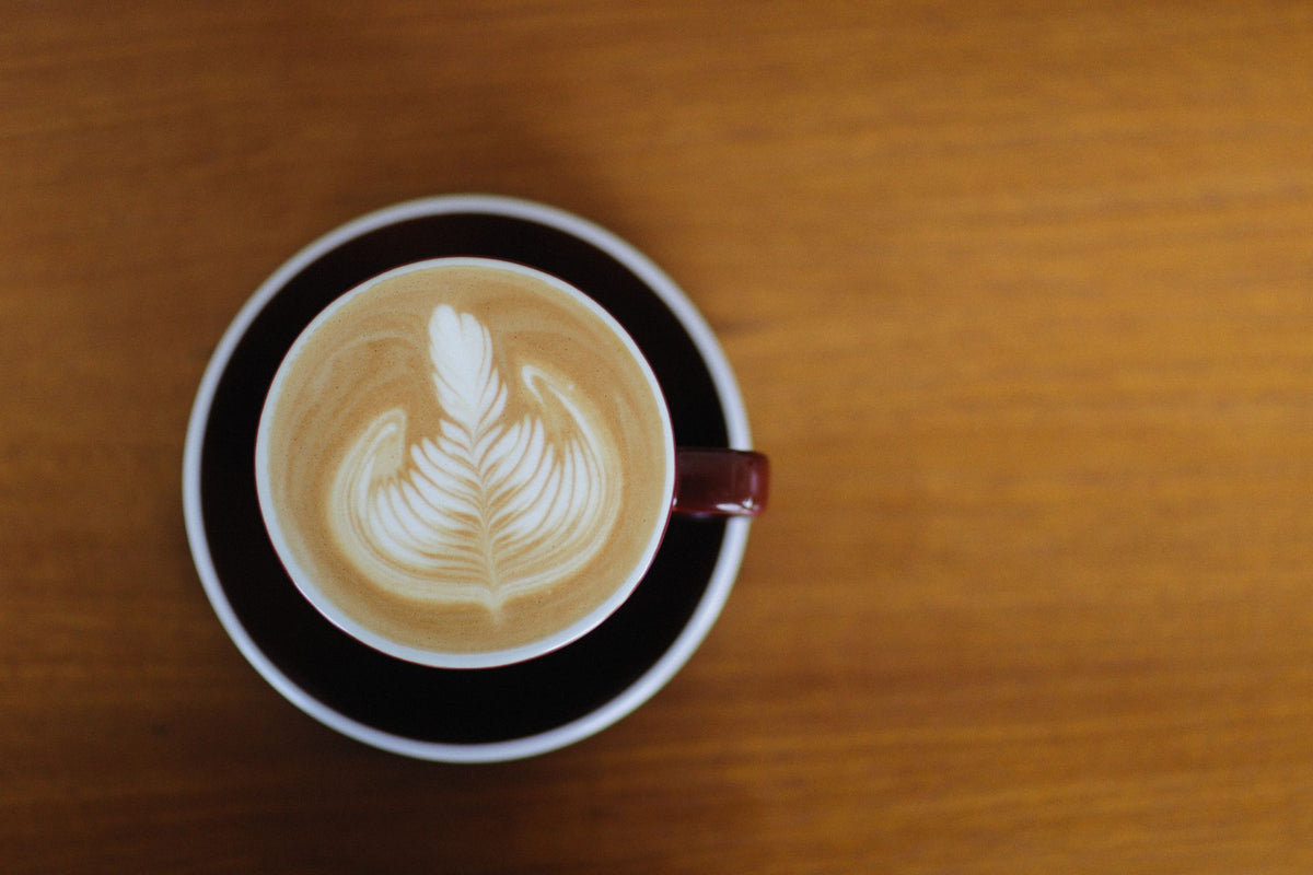 A beautifully crafted cappuccino with intricate latte art, viewed from above on a wooden table.